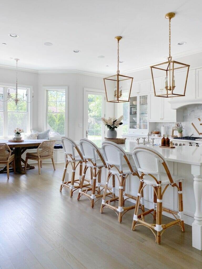 Serena & Lily Memorial Day Sale - White kitchen features Serena & Lily Riviera stools in white, brass Darlana lanterns, quartz counters, white kitchen cabinets with a marble subway tile backsplash.